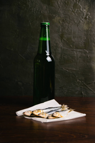 Νόστιμο σνακ μπύρα αλατισμένα αποξηραμένα ψάρια και κρύα μπύρα σε ένα γυάλινο μπουκάλι σε σκούρο φόντο. - Φωτογραφία, εικόνα