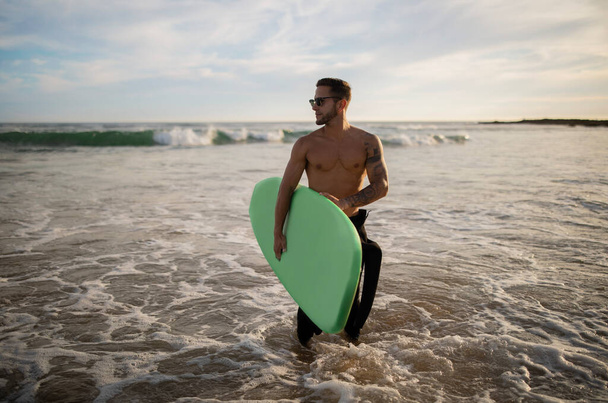 海の海岸で一人でサーフィンハンサムな筋肉男,若い男はサーフボードを保持し、離れて見て,アスレチック男性サーファー高波を待っています,ウォータースポーツを楽しむ,スペースをコピー - 写真・画像