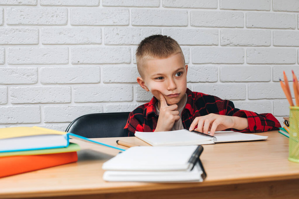 Concepto de vuelta a la escuela. Un niño en proceso de estudio se sienta en una mesa con libros, cuadernos y lápices. Vista frontal - Foto, Imagen