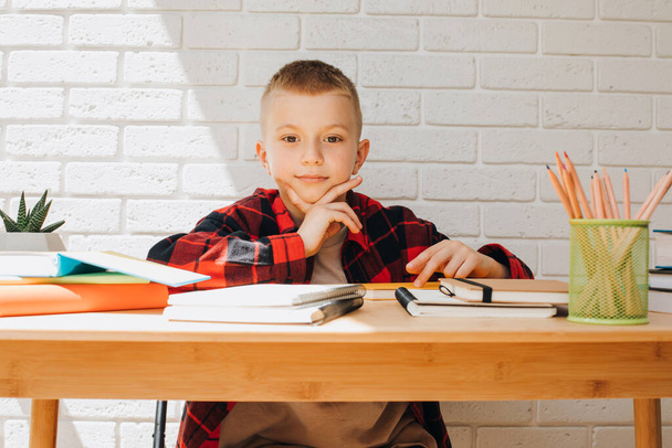 Fogantatás vissza az iskolába. Egy tanuló fiú egy asztalnál ül könyvekkel, jegyzetfüzetekkel és ceruzákkal. Előnézet - Fotó, kép