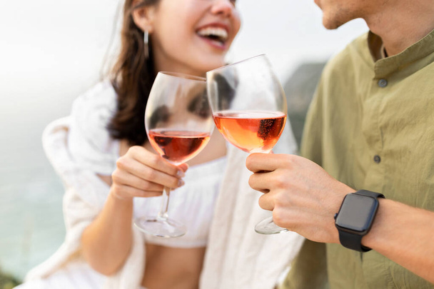 Feliz hombre y mujer clanging copas de vino con vino rosa, tener fecha y picnic en la playa, primer plano. Concepto de relaciones románticas y celebración aniversario - Foto, imagen