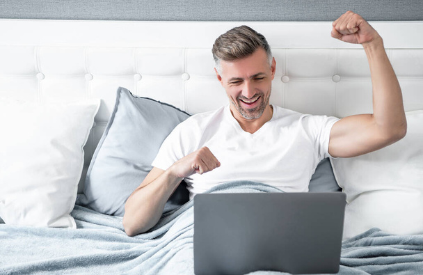 mature man working on laptop in bed. success. - Foto, afbeelding