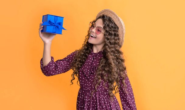 happy child with curly hair hold present box on yellow background. - Фото, изображение