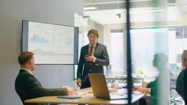 Uomo d'affari in giacca e cravatta che spiega i grafici finanziari sulla lavagna digitale e presenta al team durante la riunione dell'ufficio - Filmati, video