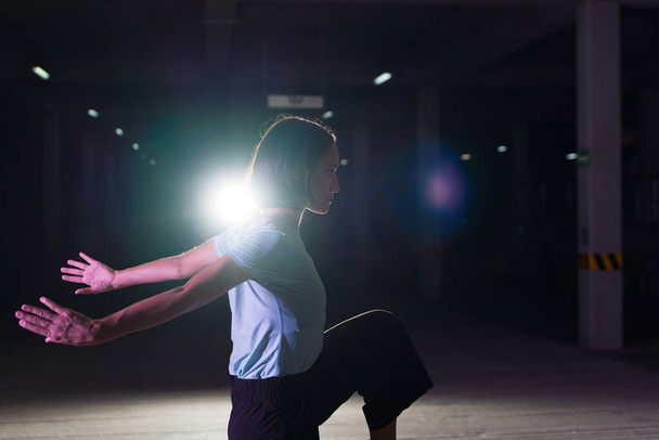 Perfil de un artista urbano en acción bailando por la noche mientras hace una danza moderna fresca en el escenario - Foto, imagen