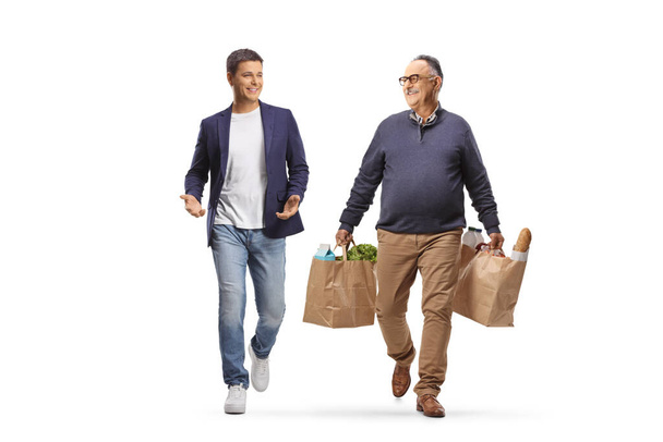 Mature man with grocery bags walking and talking to a younger man isolated on white background - Zdjęcie, obraz