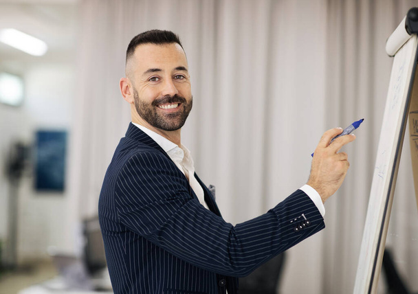 Happy handsome european adult man in suit with beard teacher writing on blackboard in office coworking interior. Successful business study, webinar, work and professional occupation - Photo, image