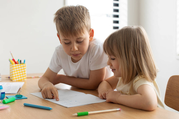 The older brother teaches the younger sister to read letters. The concept of brother and sister, home schooling. - Φωτογραφία, εικόνα