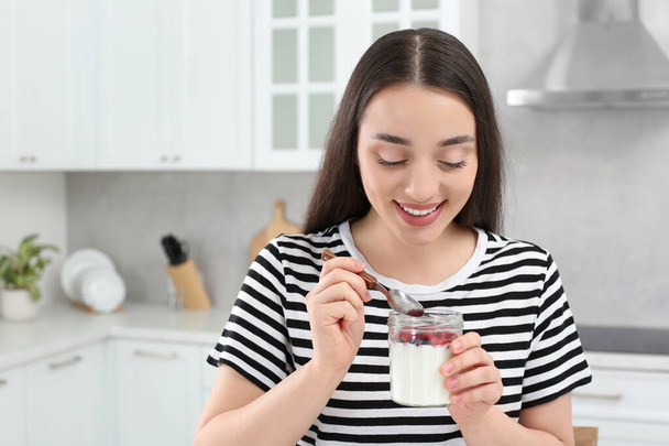 Happy woman with tasty yogurt in kitchen - Fotoğraf, Görsel