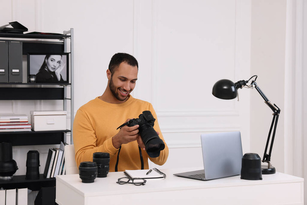 Young professional photographer with camera at table in modern photo studio - Foto, Bild