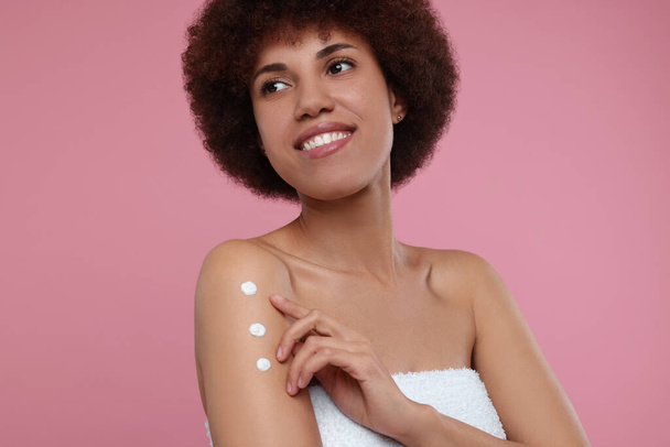 Beautiful young woman applying body cream onto arm on pink background - Foto, afbeelding