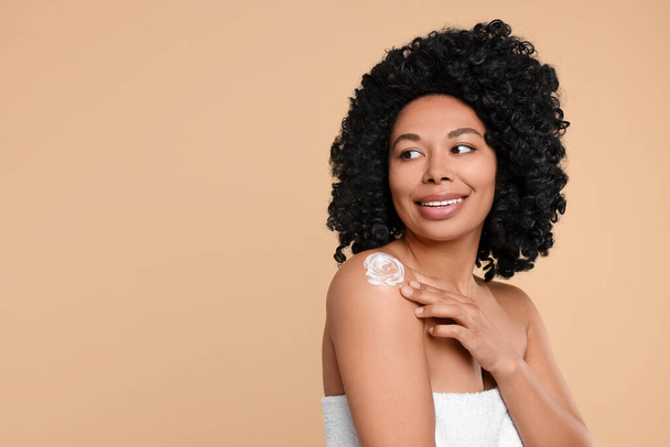 Young woman applying body cream onto shoulder on beige background. Space for text - Photo, Image