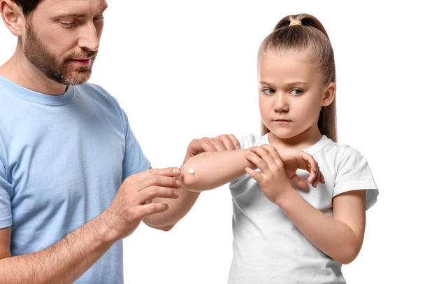 Father applying ointment onto his daughter's elbow on white background - Фото, изображение