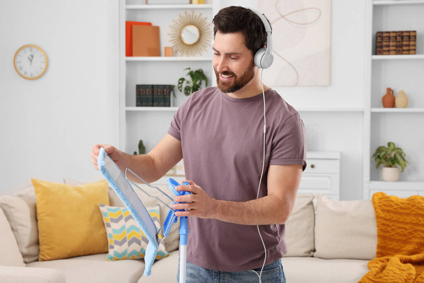 Spring cleaning. Man with headphones and mop in living room - Fotoğraf, Görsel