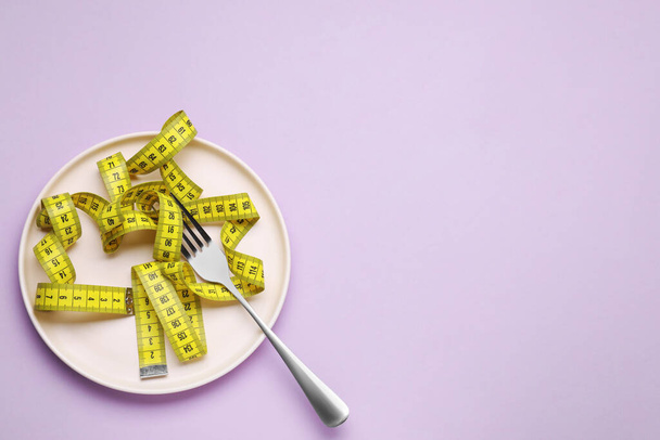 Measuring tape and fork on violet background, top view with space for text. Weight loss concept - Foto, Imagen