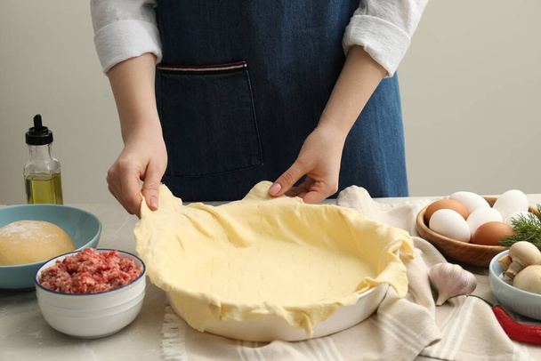 Woman putting dough for meat pie into baking dish at light grey table, closeup - Zdjęcie, obraz