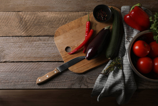 Cooking ratatouille. Vegetables, peppercorns, herbs and knife on wooden table, flat lay with space for text - 写真・画像