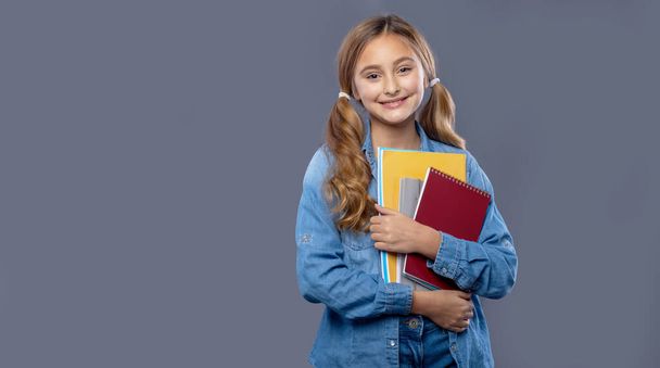 Portrait smiling little kid girl 9-10 years old jean jacket hold books isolated on gray background, studio shoot. School lifestyle concept. Education, back to school. - Photo, Image