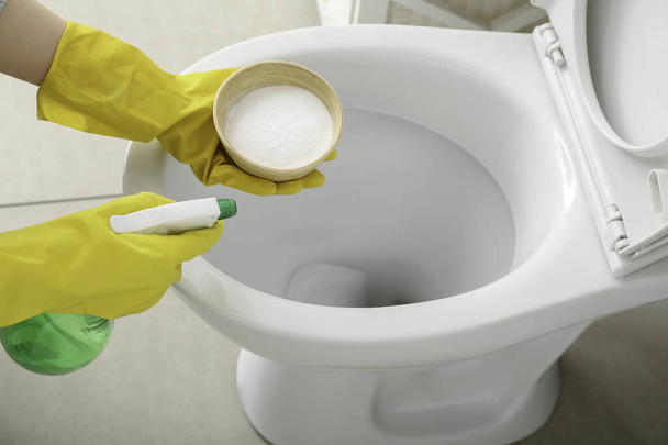 Woman in rubber gloves cleaning toilet bowl with baking soda and sprayer, closeup - 写真・画像