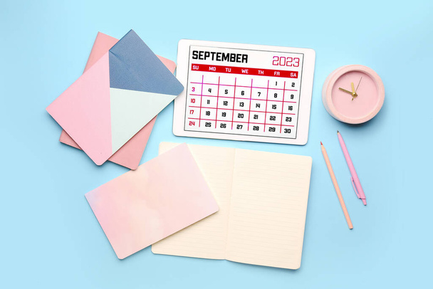 Сучасний планшетний комп'ютер з календарем, блокнотами, будильником та олівцями на синьому фоні - Фото, зображення