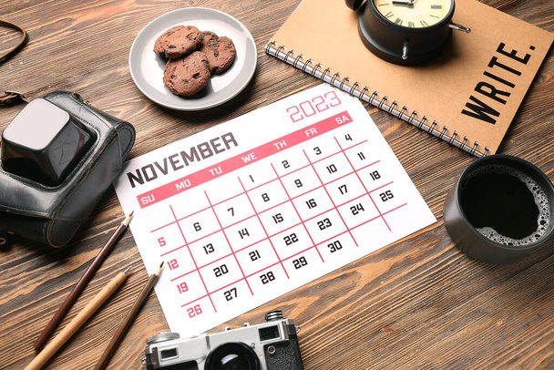 Kompozice s kalendářem, fotoaparátem, šálkem kávy a sušenkami na dřevěném pozadí - Fotografie, Obrázek