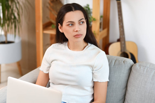 Jeune femme réfléchie avec ordinateur portable sur le canapé à la maison - Photo, image