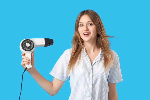 Beautiful young woman with hair dryer on blue background - Foto, Bild
