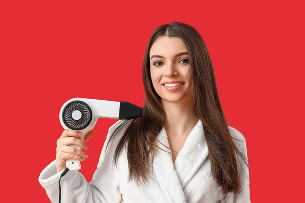 Beautiful young woman with hair dryer on red background - Photo, Image