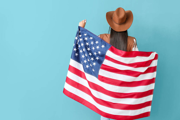 Piękna młoda kowbojka trzymająca flagę USA na niebieskim tle, widok z tyłu - Zdjęcie, obraz