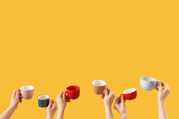 Female hands holding cups on yellow background - Foto, Imagen