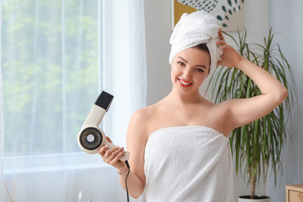 Όμορφη νεαρή γυναίκα με στεγνωτήρα μαλλιών στο μπάνιο - Φωτογραφία, εικόνα