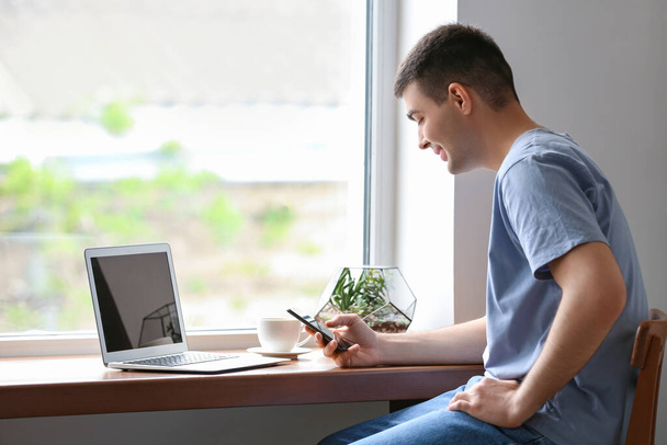 Fiatal férfi okostelefonnal ablak mellett - Fotó, kép