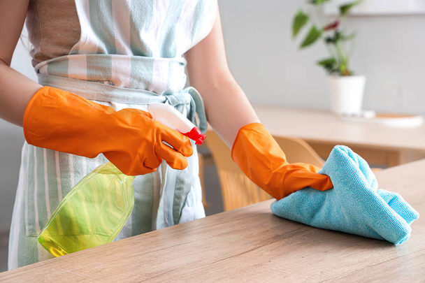 Frau in orangefarbenen Gummihandschuhen putzt Holzarbeitsplatte mit Lappen und Waschmittel - Foto, Bild