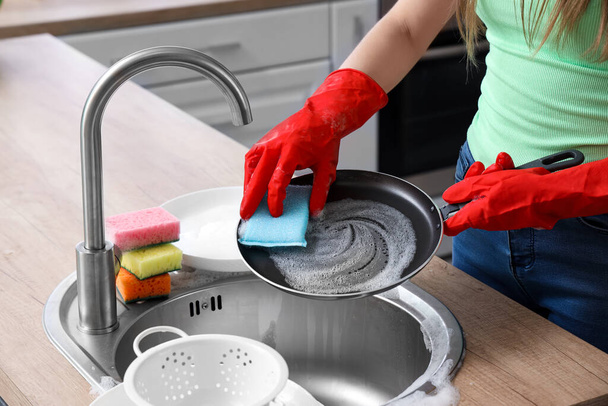 Жінка в рукавичках з червоної гуми миє сковороду з губкою - Фото, зображення