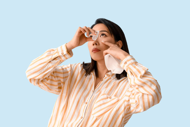 Allergic Asian woman with eye drops and tissue on blue background - Photo, Image