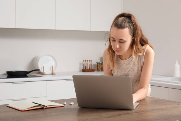 Female freelancer working with laptop at table in kitchen - Photo, Image