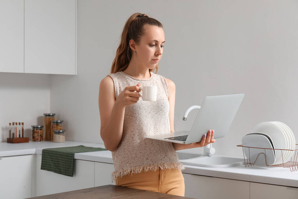 Γυναίκα ελεύθερος επαγγελματίας με φλιτζάνι καφέ και laptop που εργάζονται στην κουζίνα - Φωτογραφία, εικόνα