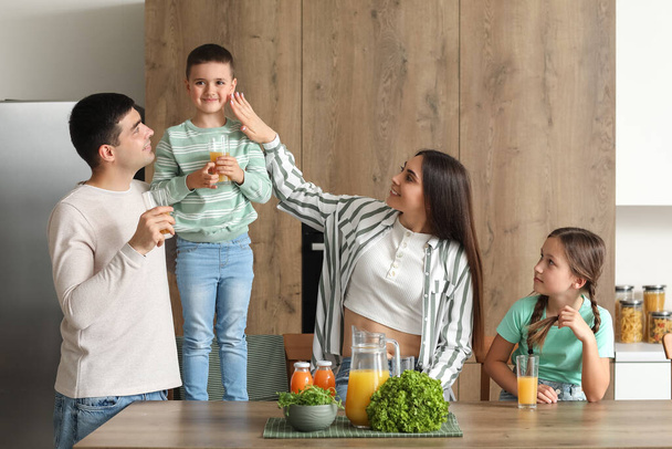 Ευτυχισμένοι γονείς με τα μικρά παιδιά τους να πίνουν χυμό πορτοκαλιού στην κουζίνα - Φωτογραφία, εικόνα