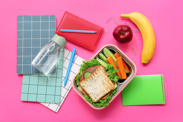 Verschillende briefpapier, drank en lunch box met lekker eten op roze achtergrond - Foto, afbeelding