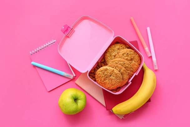 Канцелярские принадлежности и обеденная коробка с вкусной едой на розовом фоне - Фото, изображение