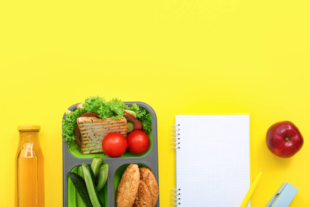 Stationery, blank notebook, drink and lunch box with tasty food on yellow background - Photo, Image