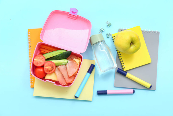 Stationery, drink and lunch box with tasty food on blue background - Photo, Image