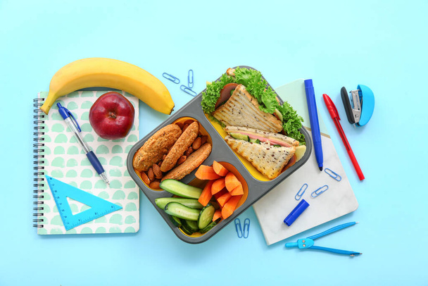 Cancelleria e cestino per il pranzo con gustoso cibo su sfondo blu - Foto, immagini