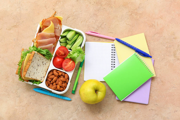 Papeterie et boîte à lunch avec des aliments savoureux sur fond orange grunge - Photo, image
