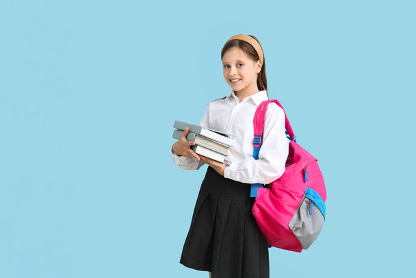 Little schoolgirl with books and backpack on blue background - Foto, Imagem