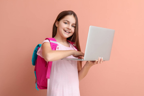 Little girl with backpack using laptop on pink background - Foto, imagen