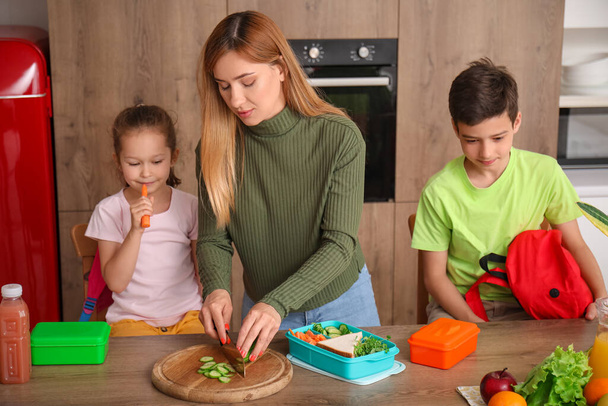 Мати готує шкільний обід для своїх маленьких дітей на кухні
 - Фото, зображення