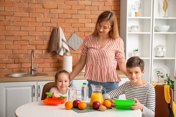 Маленькі діти зі шкільним обідом та їхня мати на кухні - Фото, зображення