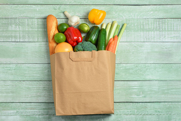 Бумажный пакет с различными продуктами на зеленом деревянном фоне - Фото, изображение