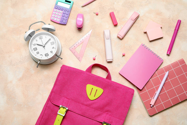 Rózsaszín iskolai hátizsák ébresztőórával, számológép és írószer bézs grunge háttér - Fotó, kép